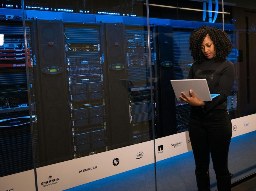 A female engineer using a laptop while monitoring data servers in a modern server room.