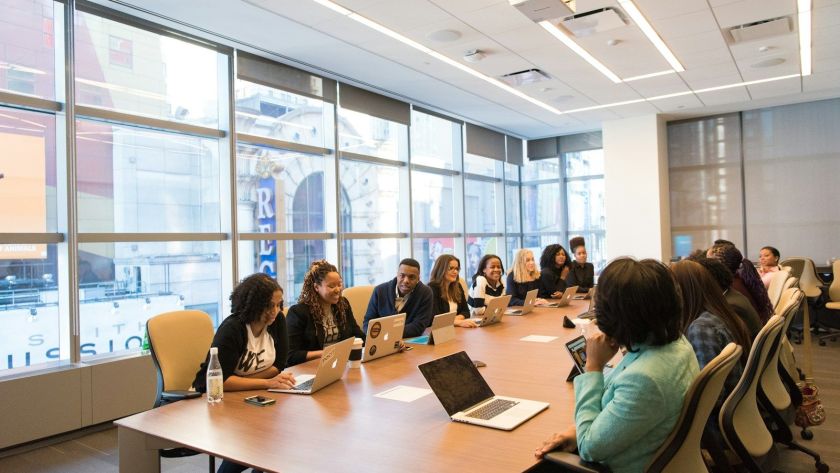 group of people sitting beside rectangular wooden table with laptops